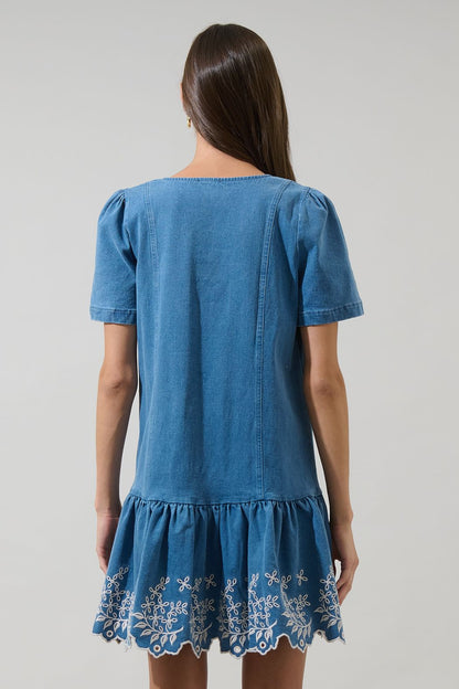 A women's medium wash blue denim short-sleeve mini dress featuring a square neckline, ruffled button placket, and cream floral embroidered scalloped hemline.