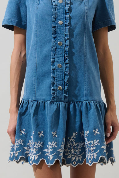 A women's medium wash blue denim short-sleeve mini dress featuring a square neckline, ruffled button placket, and cream floral embroidered scalloped hemline.